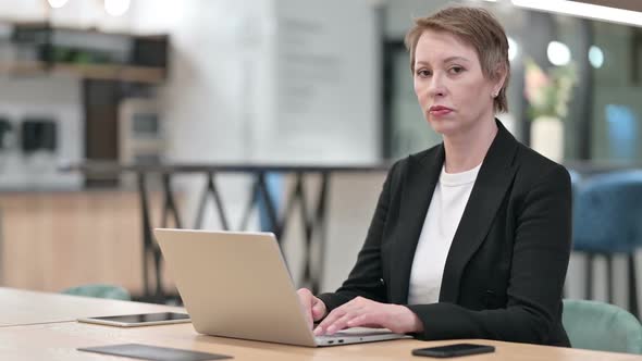 Old Businesswoman with Laptop Smiling at Camera in Office