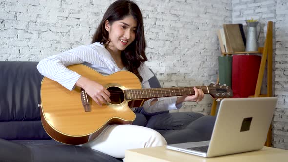 Young Asian Woman Learning How to Play Guitar on Laptop