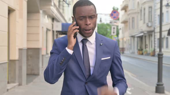 Angry African Businessman Talking on Phone While Walking on Street