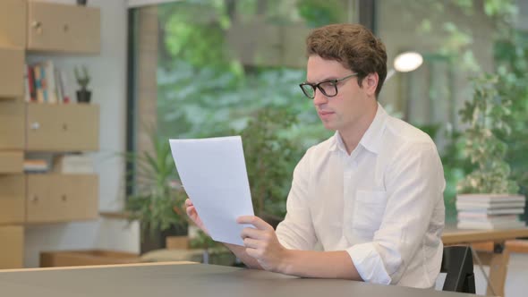 Young Man Feeling Happy While Reading Documents in Modern Office