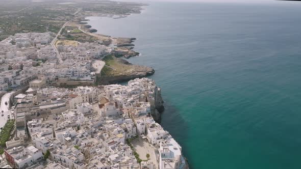 Wide aerial side to side shot showing the town of Polignano a Mare and the cliffs and sea that it si