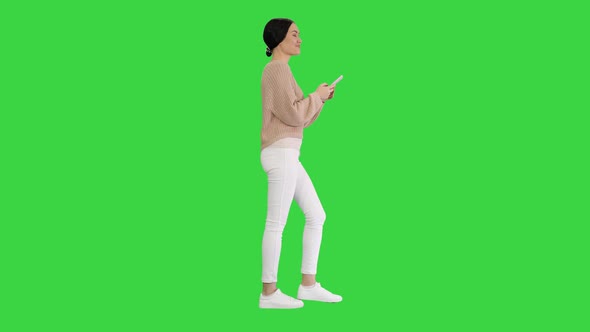 Pretty Young Female Texting on Mobile Phone While Walking on a Green Screen Chroma Key