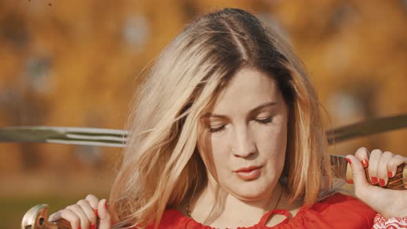 Feisty Attractive Woman in Red Clothes Standing on the Field with Her Swords Behind Her Head