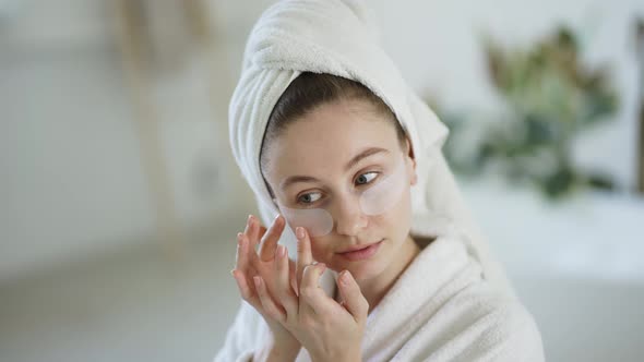 Woman at Home in a Bathrobe and Towel Applies Patches Under the Eyes