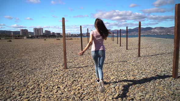 Young and Attractive Girl or Young Woman in Pink T-shirt Runing on the Beach Between Wood Pillars