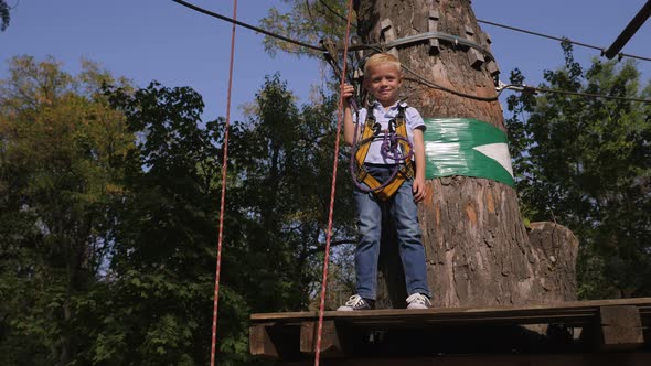 Little Happy Boy in a Rope Park Enjoys Passing Obstacles Between Trees