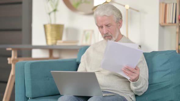 Old Man with Documents Working on Laptop on Sofa