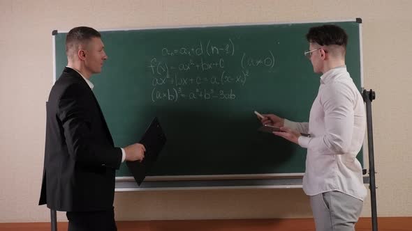 A Young Teacher Talks Near the Blackboard with a Student in the Math Room