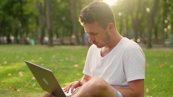 Young Man Working Using Laptop in the Park While Sitting on the Lawn