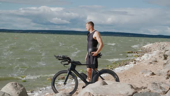 Motivation Pro Racer Stand Near the Lake Holding a Bicycle Helmet in His Hands a Cyclist in Training