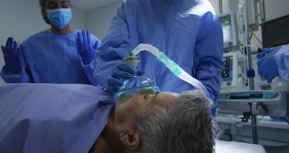 Mixed race surgeons wearing protective clothing putting patient to sleep in operating theatre