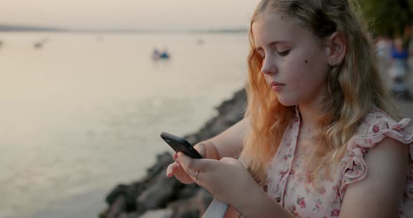 Young Girl Texting on a Phone on Path By the Sea
