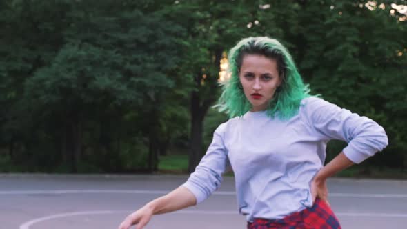 Young Stylish Funky Girl with Green Hair Riding Roller Skates and Dancing in Park Slow Motion