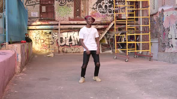 A young black guy is dancing on the street in a bad neighborhood