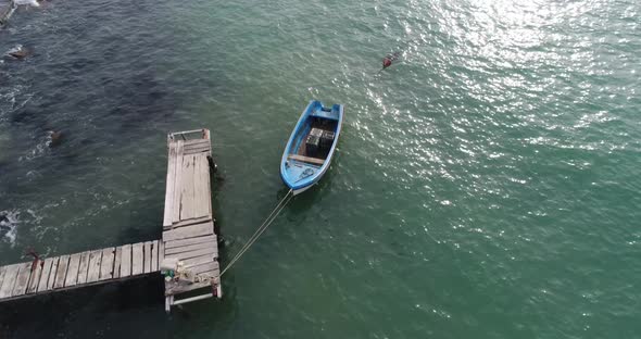4k aerial video of lonely fishing boat and wooden pier in turquoise ocean, sea.