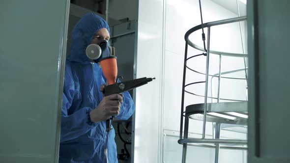 Professional painter in a protective uniform paints metal structures with an airbrush