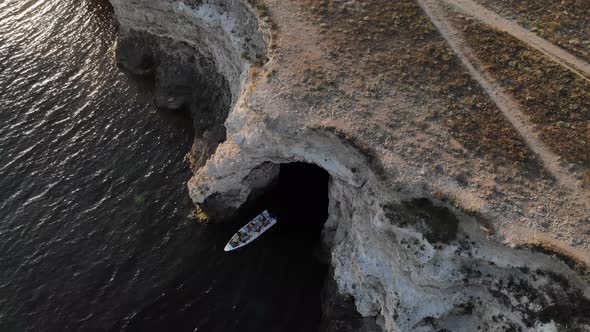 Aerial View of a Motor Boat with Tourists Sails Out of a Rocky Cave on the Coast of the Ocean in the