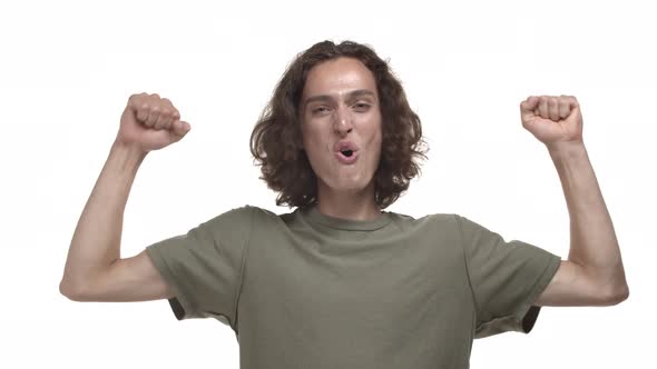 Handsome Young Man with Wavy Hair Wearing Casual Tshirt Triumphing and Winning Something Raising