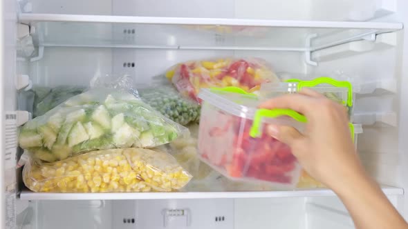Female Hands take out containers with frozen vegetables in the fridge.
