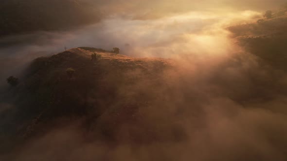 4K aerial view over mountain at sunrise in heavy fog. golden morning sunlight