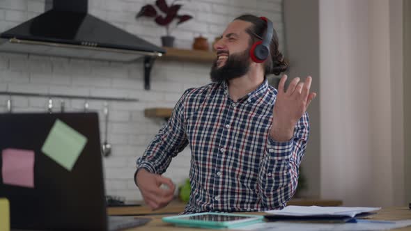 Cheerful Middle Eastern Bearded Man in Headphones Imitating Guitar Playing Enjoying Music on Break