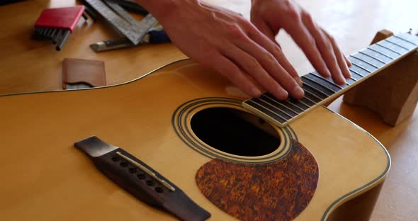 Close up hands of a luthier craftsman measuring an acoustic guitar neck fretboard on a wood workshop