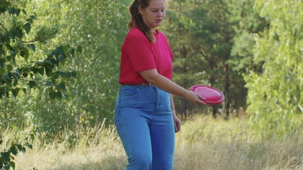 Young Plump Woman Playing with Her Dog Outdoors  Throwing a Red Plastic Disk for Her Dog to Catch