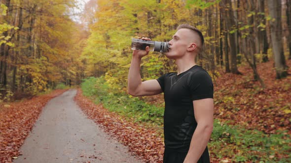 The Athlete is Standing on a Forest Road and Drinking Water From a Bottle