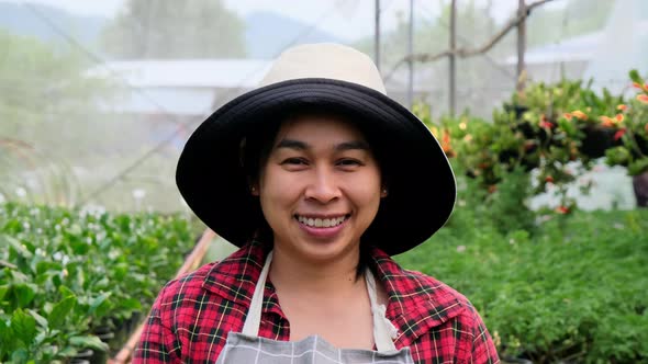 Smiling gardener wearing an apron and looking at the camera in a greenhouse.