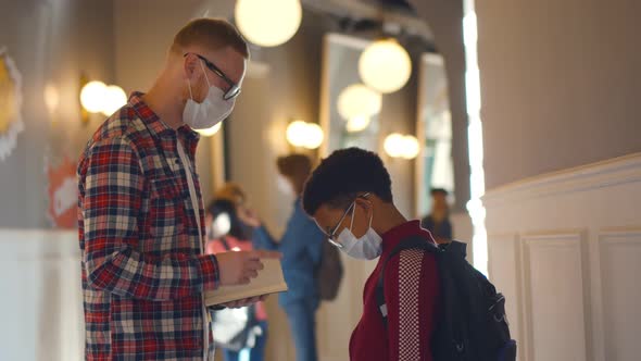 Side View of Young Teacher in Mask Scolding African Schoolboy for Bad Behavior