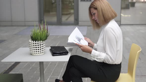 A young business woman is looking at documents for a new project outdoors. Business growth charts.