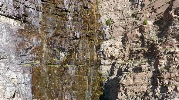 A small waterfall in Ogden Canyon, Utah trickles down craggy rocks as seen by an ascending drone fro