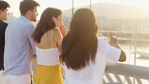 Young Multiracial Friends Enjoying Amazing Sunset While Standing on Bridge in Seaport and Talking