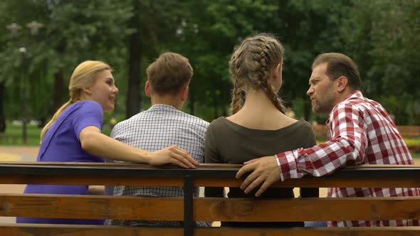 Cheerful Parents and Their Teenage Children Planning Weekend on Bench in Park