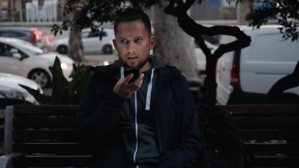 Casual Happy Man Using Smartphone Sitting on a Bench in Park Tourist Use Voice Recognition Ai Speech