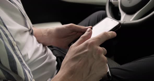 Close up of man typing and tapping on smartphone while in car.