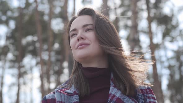 Portrait of Confident Brunette Lady Looking Away and Smiling As Standing in Forest in Sunrays. Happy