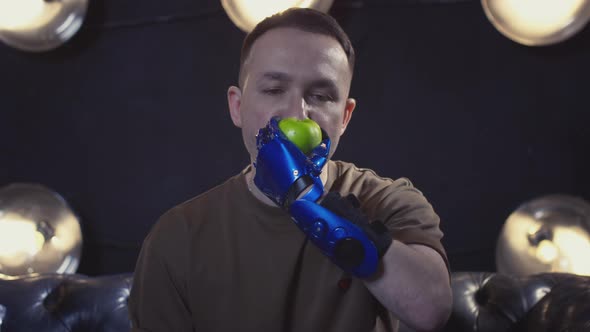 A Disabled Man with a Prosthetic Hand is Biting a Green Apple