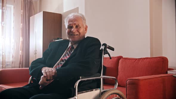 Elderly Grandfather - Smiling Grandfather Is Sitting in a Wheelchair and Looking at the Camera