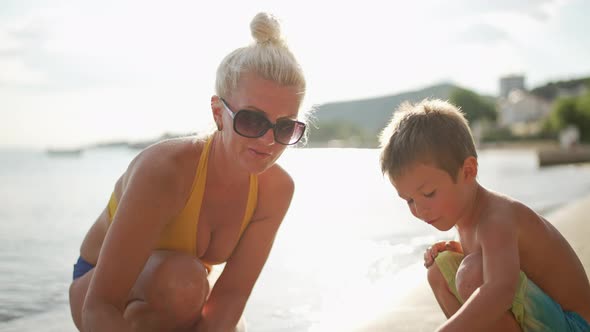 Mother and Son are Playing on the Beach Near the Sea on Vacation in Summer