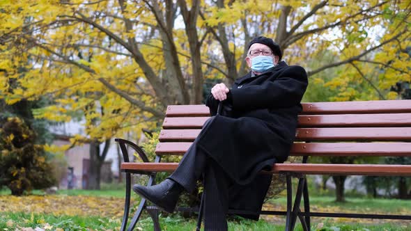 An Old Sad Grandfather is Sitting on a Bench in a Park in New York