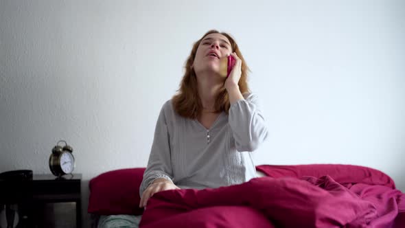 Young Woman Sitting on the Bed in Pajamas Talking on the Mobile Phone