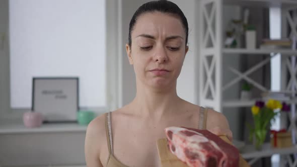 Young Slim Vegetarian Woman with Nausea Looking at Raw Meat Indoors