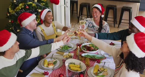Happy group of diverse friends in santa hats celebrating meal, toasting with vine at christmas time