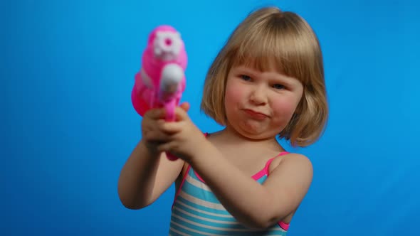 Little Blond Girl with Short Hair in a Swimsuit is Playing with Pink Water Gun