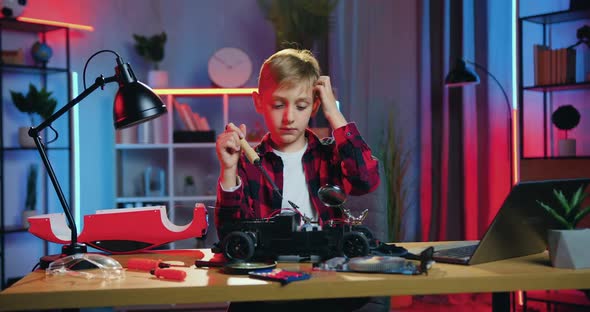 Teen Boy Sitting in front of His Broken Toy Car and Trying to Fix Small Details with Soldering Iron