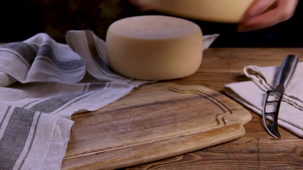 Women hands put a wheel of  fresh homemade cheese on a wooden board close up