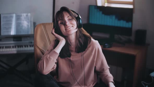 A beautiful girl with headphones listens to music in a chair at the computer. Dancing and smiling.