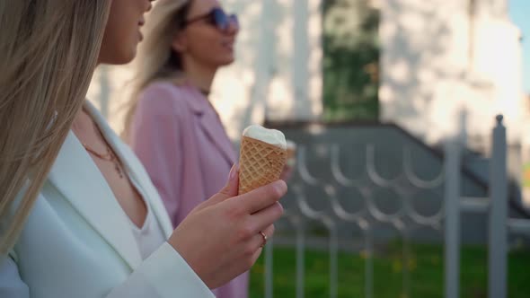 Two young adult females walking with ice cream. Girlfriends spend time together outdoors