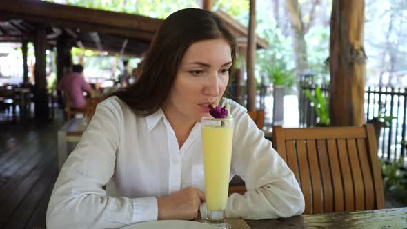 Young Woman Drinks a Fruit Cocktail in a Cafe